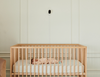Baby slaapt op de rug in een houten bedje, met een babyfoon met camera aan de muur erboven