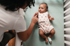 Een ouder legt een baby op de rug in het bedje; aan het voetje zit de Dream Sock