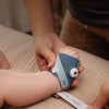 Een ouder doet een baby een stoffen sokje in Bedtime Blue aan